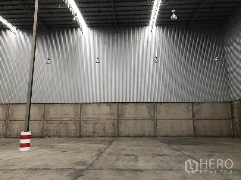 Warehouse for rent in Lam Luk Ka, Pathum Thani - Close-up of corrugated steel wall, high-bay lights and reinforced concrete flooring.