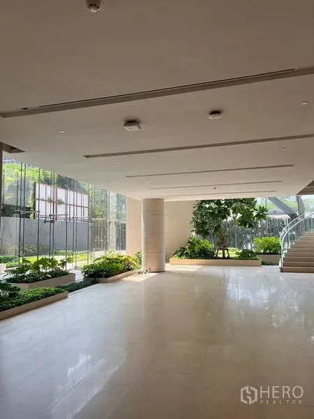 Retail Space for rent - Bright retail lobby area with large windows, ceiling lights, lush planter boxes and a sweeping staircase beside round columns.