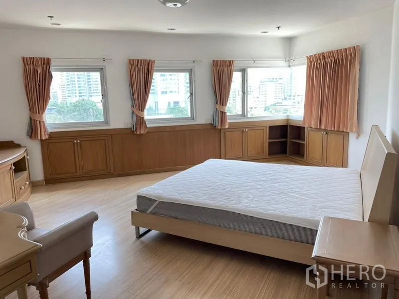 Condominium for rent in Khlong Toei, Bangkok - Corner master bedroom with multiple windows, built-in cabinetry, and city outlook.