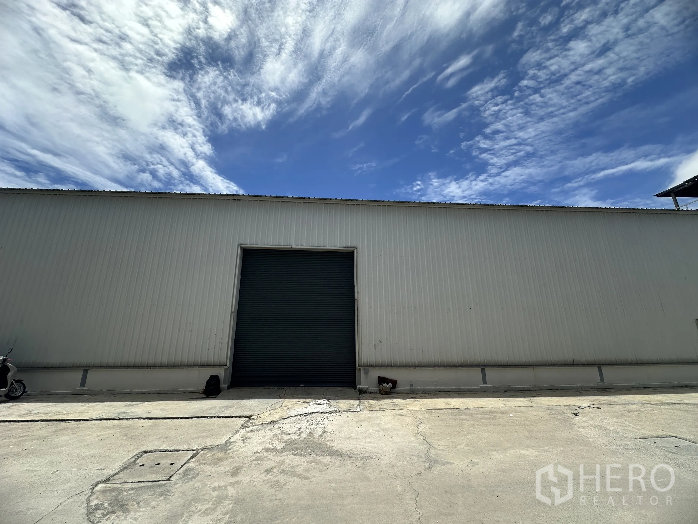 Factory for rent in Mueang Samut Prakan, Samut Prakan - Metal-clad factory exterior with large roller shutter door and concrete yard under a blue sky.