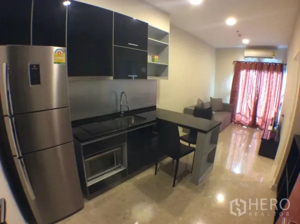 Condominium for rent in Khlong Toei, Bangkok - Compact black kitchenette with breakfast bar, stainless fridge, and open-plan living area.