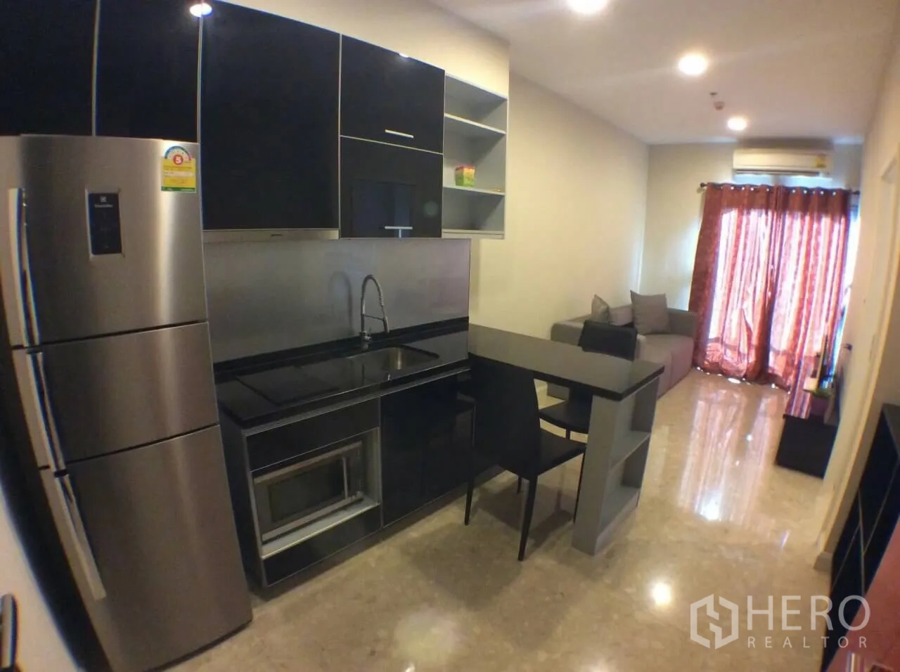 Condominium for rent in Khlong Toei, Bangkok - Compact black kitchenette with breakfast bar, stainless fridge, and open-plan living area.