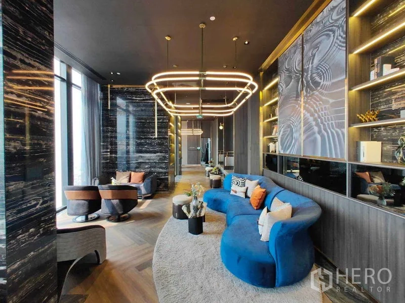 Condominium for rent in Watthana, Bangkok - Stylish lounge with a blue curved sofa, shelving, and contemporary lighting.