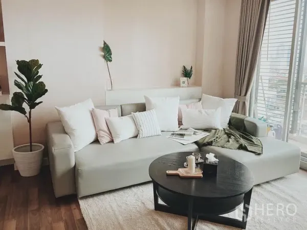 Condominium for rent in Thon Buri, Bangkok - Light-filled living room with large sofa, balcony doors and hardwood floors.