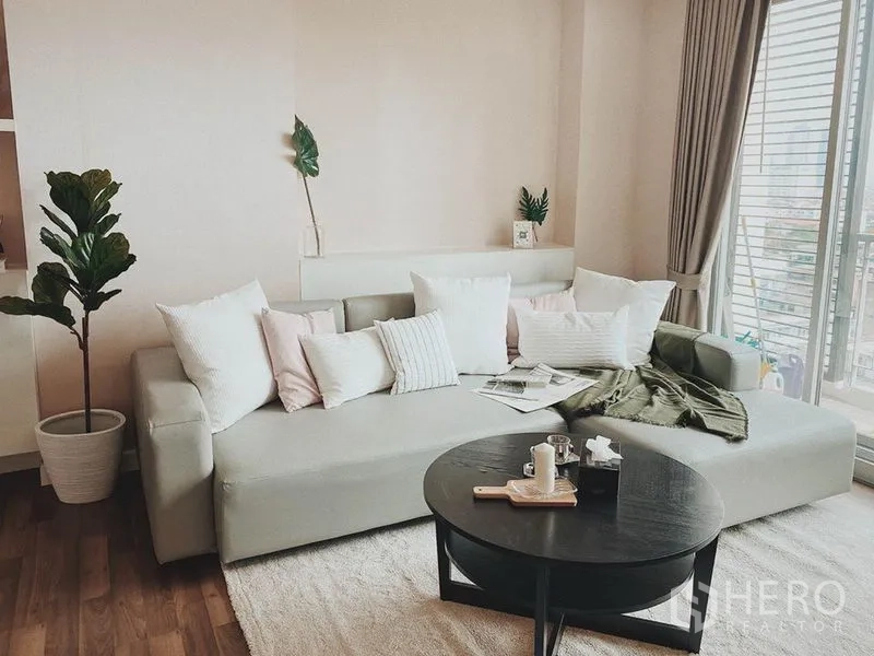 Condominium for rent in Thon Buri, Bangkok - Light-filled living room with large sofa, balcony doors and hardwood floors.