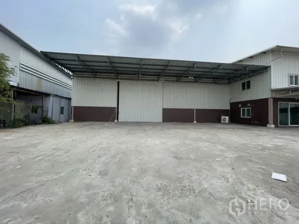 货栈 出租在Lat Lum Kaeo, Pathum Thani - 仓库立面正面视角，设高卷门与深雨棚装卸区。