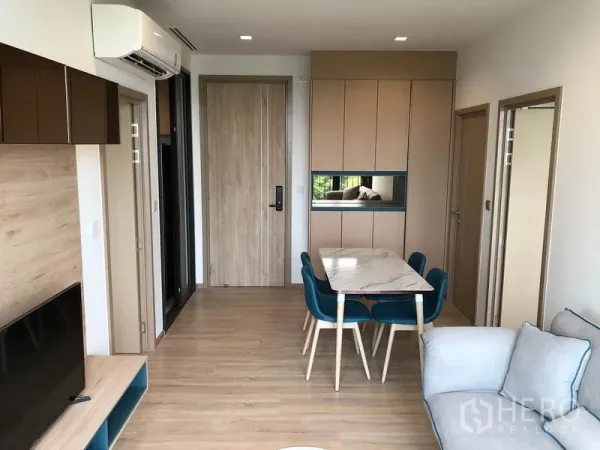 Condominium for rent in Watthana, Bangkok - Dining area with marble table, teal chairs, built-in cabinetry and entry door on light wood flooring.