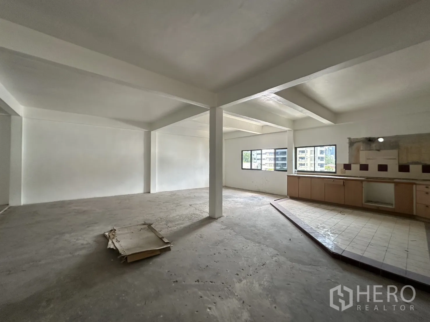 Retail Space for rent in Watthana, Bangkok - Open-plan retail floor with white walls, columns, windows, and a raised tiled counter with cabinets.