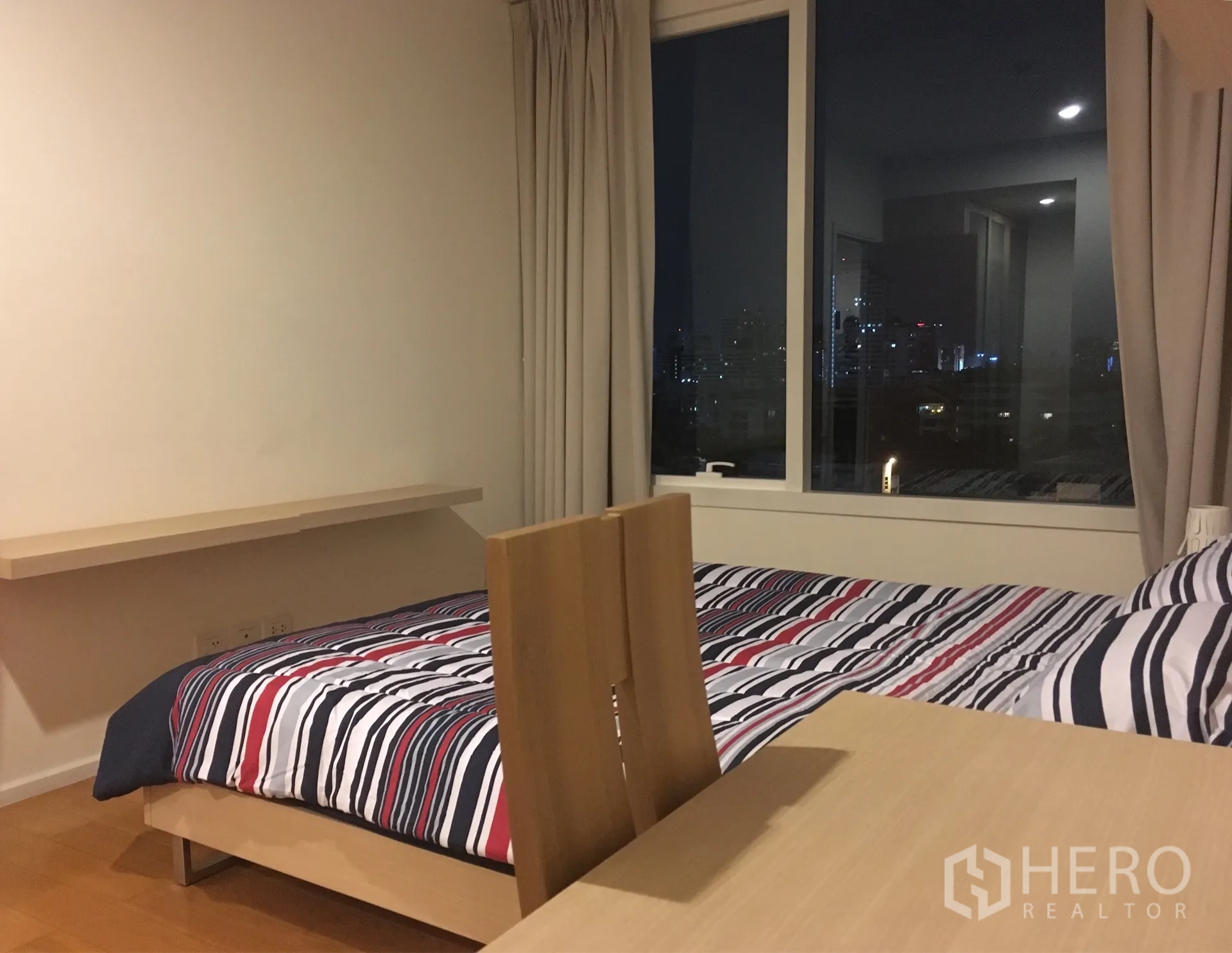 公寓 出租在Watthana, Bangkok - 卧室配条纹床品与书桌，落地窗可欣赏曼谷夜景