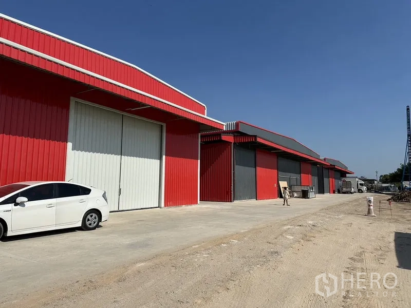 Warehouse for rent in Lam Luk Ka, Pathum Thani - Row of modern warehouses with large roller shutter doors and parking along a private access road.