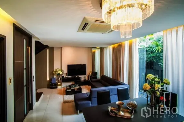 联排别墅 出租或出售在Watthana, Bangkok - 开放式客厅，转角沙发与水晶吊灯，落地窗望向小花园