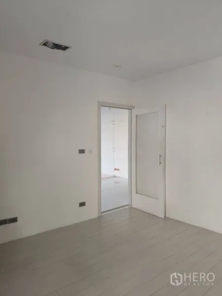 办公空间 出租在Khlong Toei, Bangkok - 极简白色房间，木纹地板，玻璃门通向相邻的瓷砖办公区。