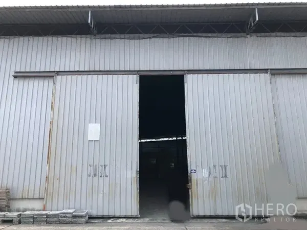 คลังสินค้า ให้เช่าในPak Kret, Nonthaburi - ด้านหน้าคลังสินค้า ประตูบานเลื่อนเปิดบางส่วน พร้อมลานคอนกรีต