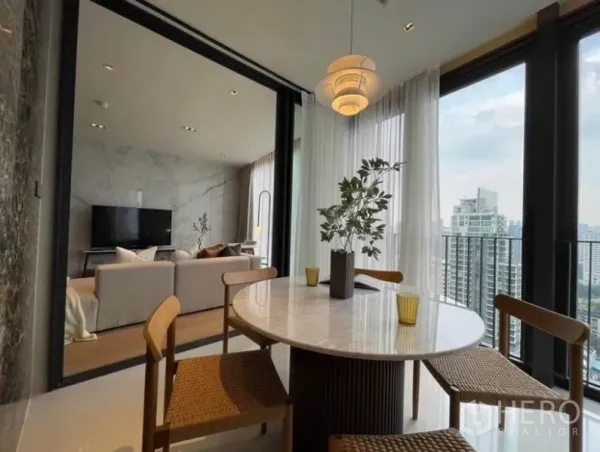 Condominium for rent or sale in Khlong Toei, Bangkok - Dining nook with round marble table and pendant light opening to a balcony overlooking the skyline.