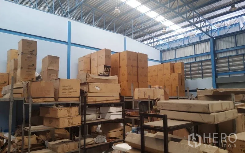 Warehouse for sale in Mueang Nonthaburi, Nonthaburi - High-ceiling warehouse interior with stacked cartons and a steel truss roof.