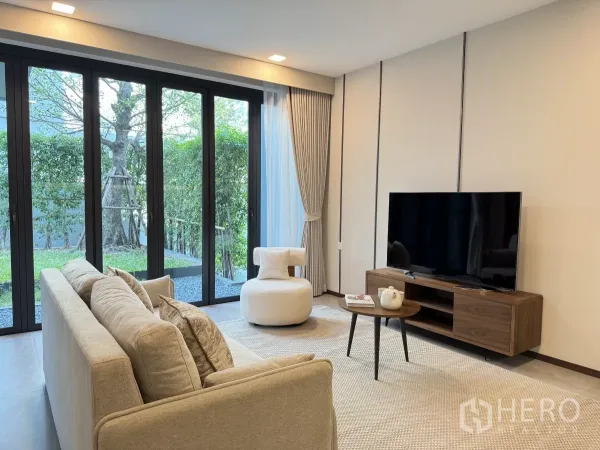 บ้าน ให้เช่าในSaphan Sung, Bangkok - ห้องนั่งเล่นสว่างด้วยประตูกระจกเต็มบาน โซฟาสีเบจ ตู้ทีวี มองเห็นสวนเขียว