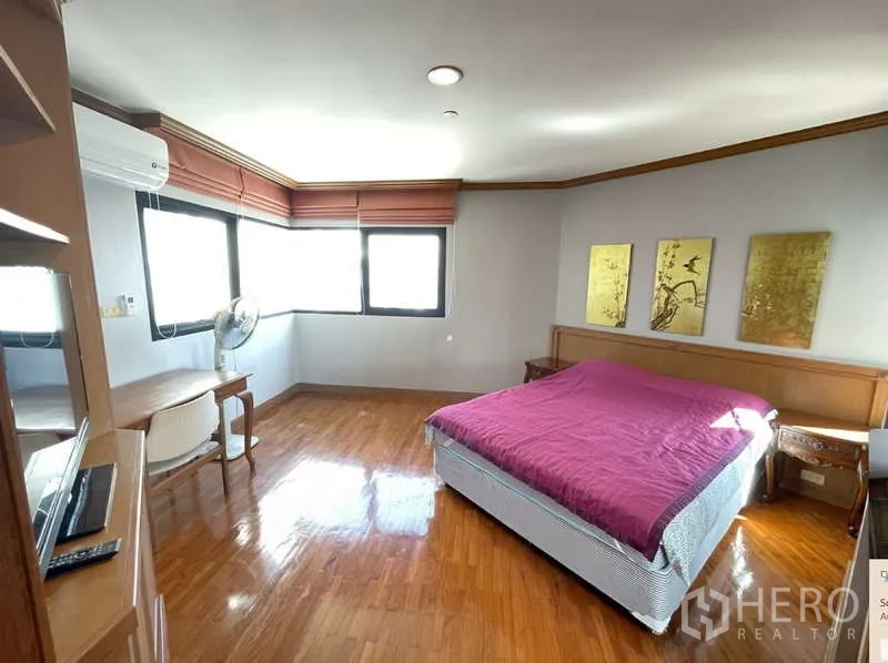 Condominium for rent - Corner bedroom with multiple windows, desk and a bed with magenta cover.