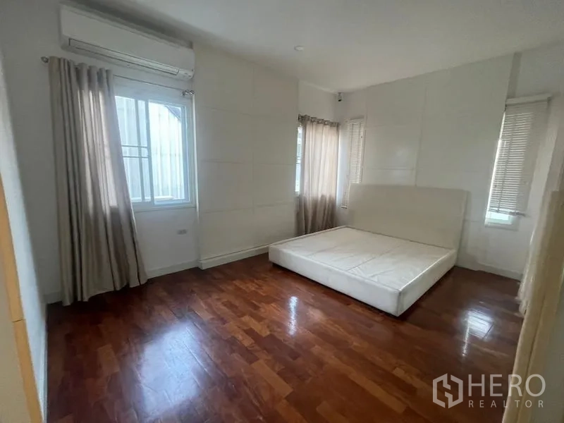 Detached House for rent or sale in Khan Na Yao, Bangkok - Spacious master bedroom with corner windows, wood floors and an upholstered bed base.