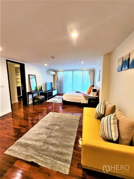 Condominium for rent in Bang Rak, Bangkok - Master suite view showing yellow sofa, walk-in closet, and large window.