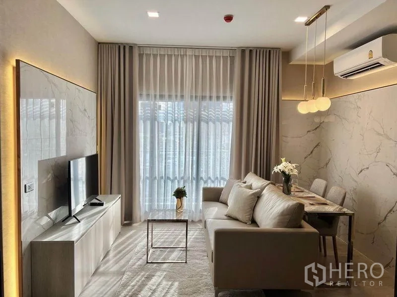 Condominium for rent in Watthana, Bangkok - Compact living and dining area with sofa, TV and pendant lights by sheer curtains.