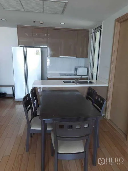 Condominium for rent in Khlong Toei, Bangkok - Dining table for four beside a compact kitchen with glossy cabinetry.