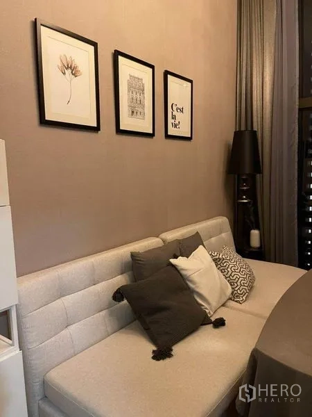 Condominium for rent in Ratchathewi, Bangkok - Cozy sofa with cushions and framed wall art beside long curtains in the living area.