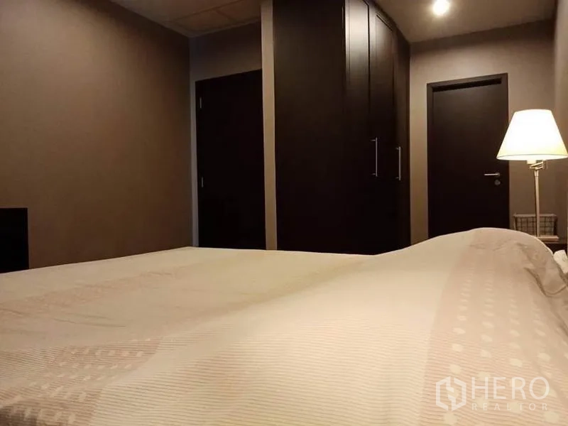 Condominium for rent in Sathon, Bangkok - Bedroom showing built-in dark wardrobes, soft lighting and entry doors.