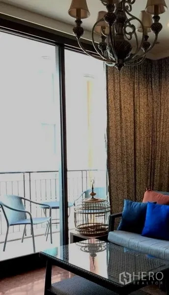 Condominium for rent in Khlong Toei, Bangkok - Living area opening to a balcony with outdoor chairs and large sliding doors with drapes.