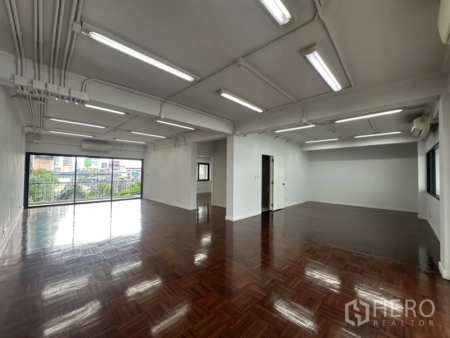 办公室 for rent in Watthana, Bangkok - 宽敞开放式办公室，亮面木地板，顶置长条灯，落地推拉门通向阳台并享城市景观。
