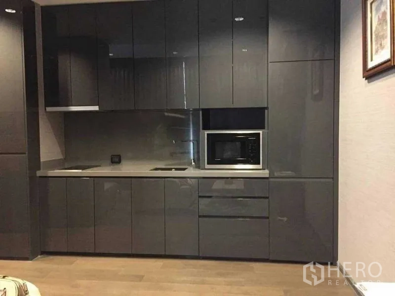 Condominium for rent in Bang Rak, Bangkok - Sleek grey kitchenette with ample cabinets, cooktop, sink, and microwave.
