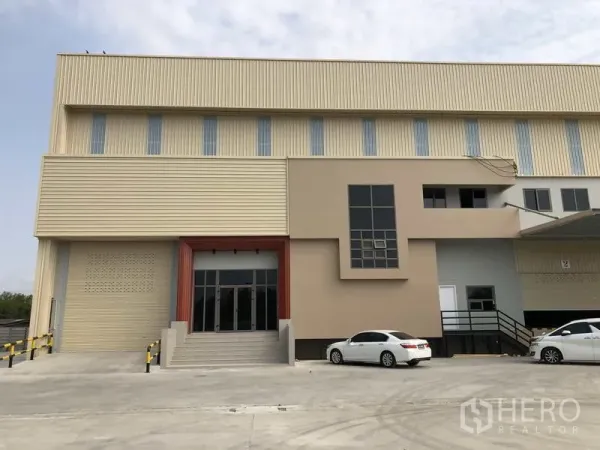 Factory for rent or sale in Samut Prakan - Front facade of the factory showing the office block, glazed entrance, and parking area.