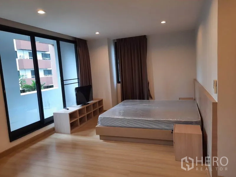 Condominium for rent in Watthana, Bangkok - Spacious master bedroom with sliding glass doors to a balcony, queen bed, TV console and recessed lighting.