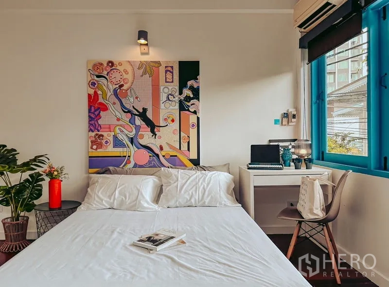带办公室的家 出租在Watthana, Bangkok - 卧室配白色床品、色彩艺术画、窗边书桌与蓝色窗框。