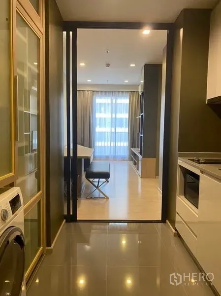 Condominium for rent in Watthana, Bangkok - Hallway with sliding glass partition opening to a bright living room with balcony curtains and built-in shelving.