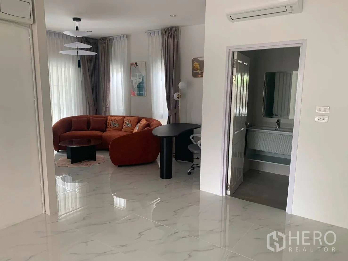 บ้านเดี่ยว for rent in Bang Phli, Samut Prakan - พื้นที่นั่งเล่นสว่างด้วยโซฟาทรงโค้งสีส้ม โต๊ะทำงาน และห้องน้ำใกล้เคียง.