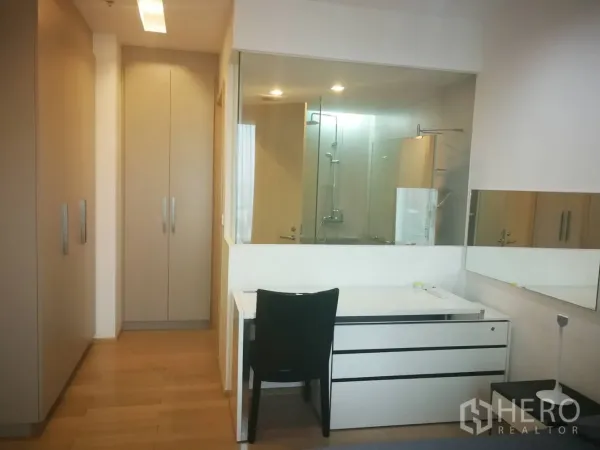 Condominium for rent in Khlong Toei, Bangkok - Walk-through wardrobe and study area leading to a glass-walled bathroom with a modern shower.