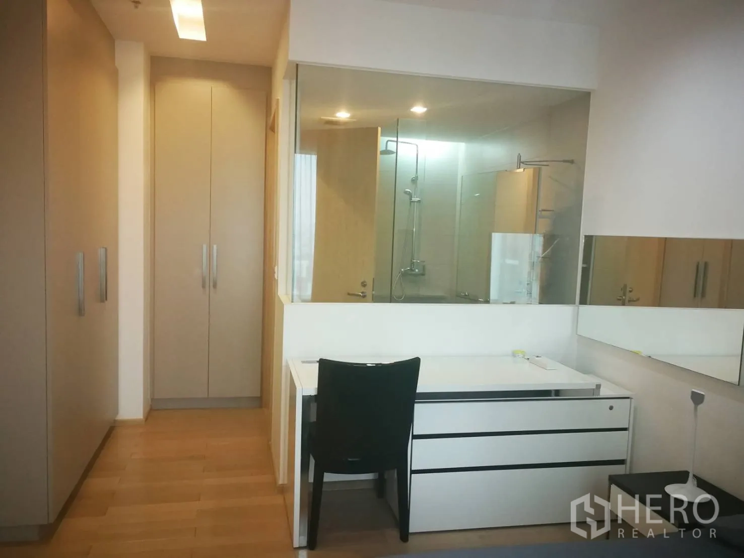 Condominium for rent in Khlong Toei, Bangkok - Walk-through wardrobe and study area leading to a glass-walled bathroom with a modern shower.