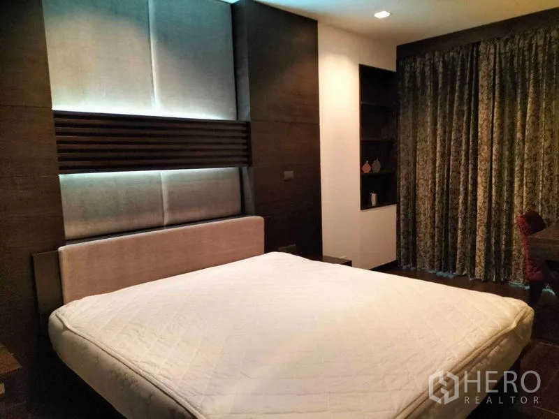 Condominium for rent in Ratchathewi, Bangkok - Primary bedroom with upholstered headboard, backlit wall panels and floor-length curtains.