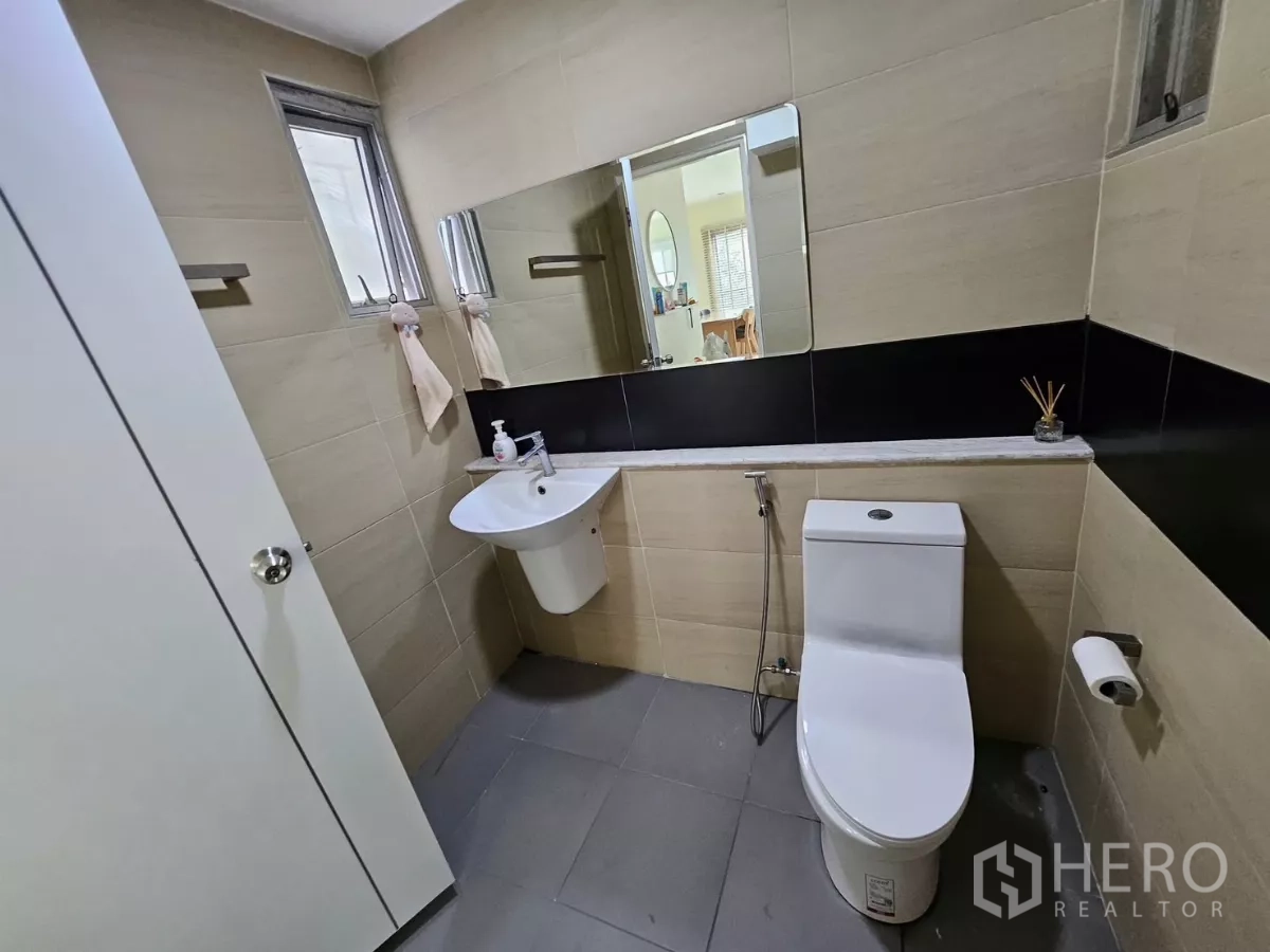 Detached House for rent in Khlong Toei, Bangkok - Second bathroom with beige tiles, wall mirror, corner basin and toilet.