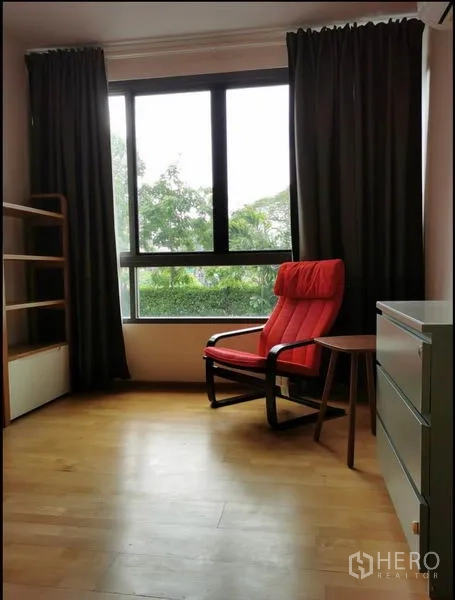Condominium for rent in Khlong Toei, Bangkok - Bright room with red lounge chair, large window, and green outlook.