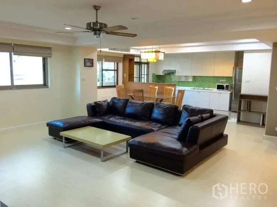 公寓 出租在Watthana, Bangkok - 开放式客厅，黑色L型真皮沙发、用餐区与带绿色马赛克背墙的现代厨房。