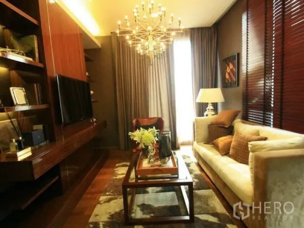 Condominium for rent or sale in Watthana, Bangkok - Warm-toned living room with chandelier, cream sofa, wooden shelving, TV and tall curtains in a Thonglor condo.