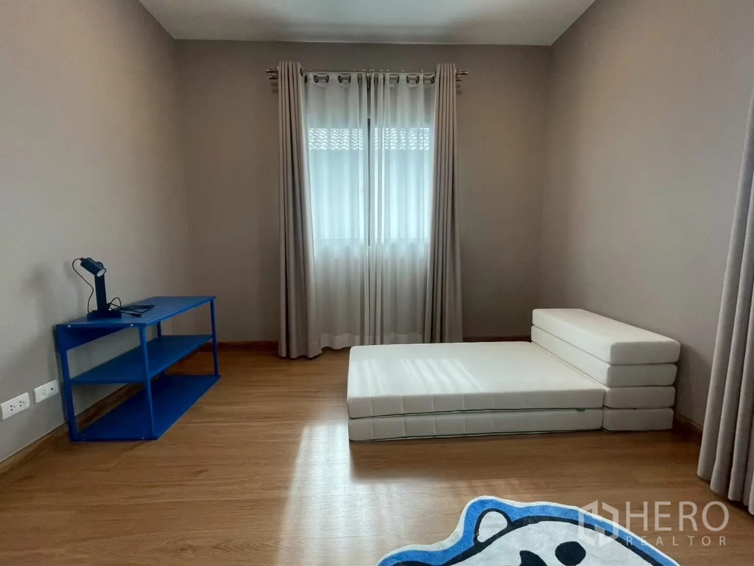 บ้านเดี่ยว for rent in Bang Phli, Samut Prakan - ห้องนอนมินิมอลพร้อมที่นอนพับตั้งพื้น โต๊ะสีน้ำเงิน และหน้าต่างผ้าม่าน.
