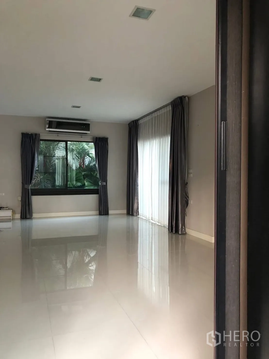 Detached House for rent in Prawet, Bangkok - Living room featuring wide windows, sheer curtains and reflective floor tiles.