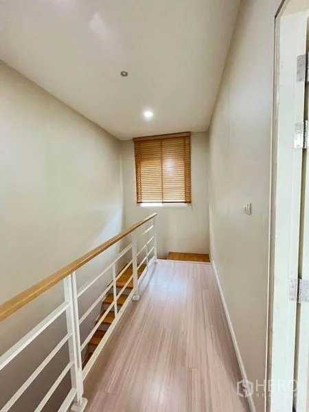 Townhouse for sale in Bang Kapi, Bangkok - Upper hallway with white metal railing, wooden handrail, and a window with blinds.