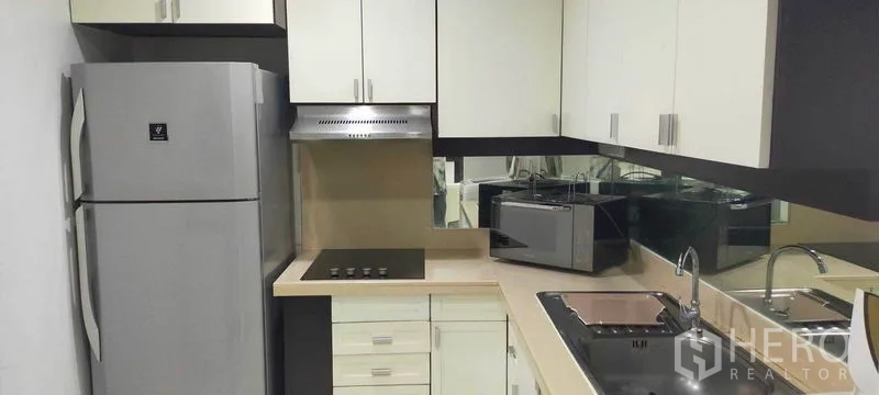 Condominium for rent in Watthana, Bangkok - Separate kitchen with fridge, electric cooktop, sink, and white cabinets.