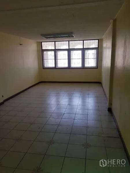 Retail Space for rent in Khlong Toei, Bangkok - Spacious tiled room with a large window fitted with security grilles and overhead lighting.