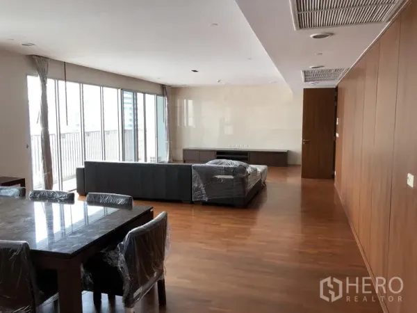 房间 出租在Watthana, Bangkok - 宽敞的客餐一体空间，落地窗与木地板，带阳台景观的现代曼谷公寓客厅。