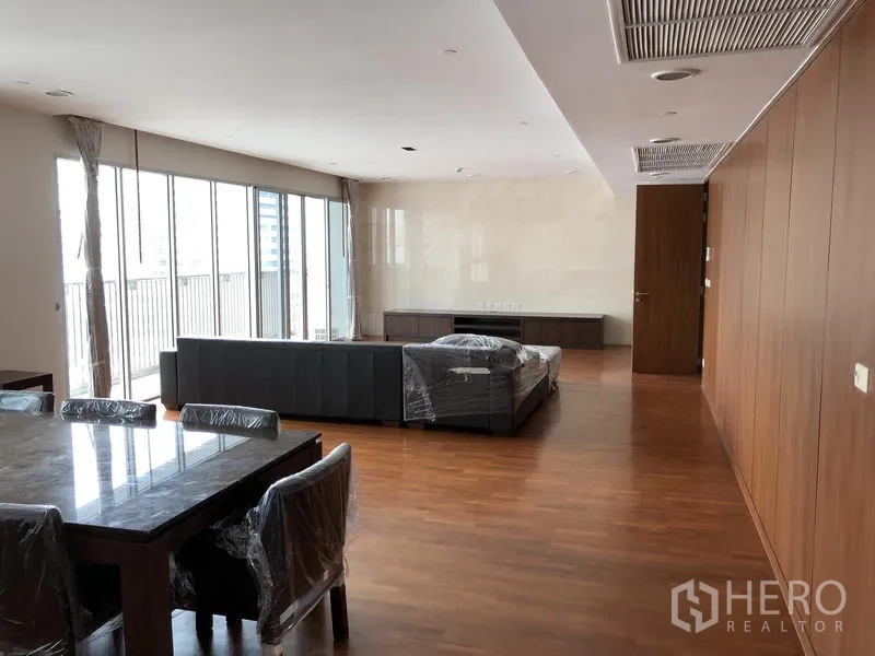 房间 出租在Watthana, Bangkok - 宽敞的客餐一体空间，落地窗与木地板，带阳台景观的现代曼谷公寓客厅。