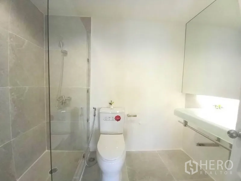 公寓 出租在Khlong Toei, Bangkok - 浴室采用玻璃淋浴间、马桶与宽镜面台盆，浅色瓷砖。